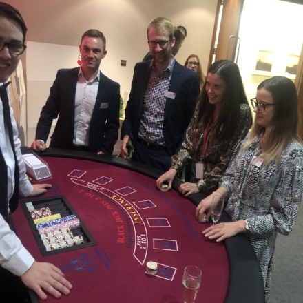 Two young women and three young men, one acting as dealer, stand around a card table