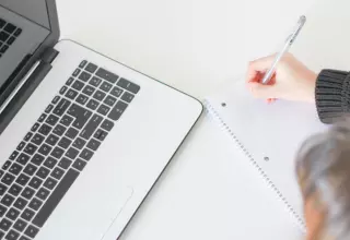Person writing in their notebook whilst using a laptop