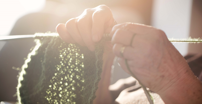 Elderly person knitting green wool